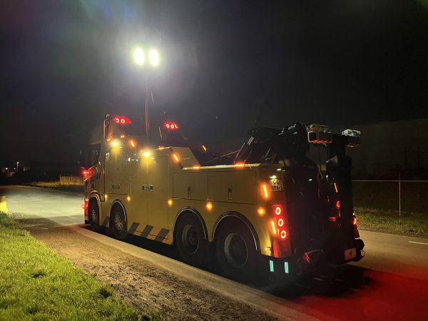 Rear of a yellow recovery truck with its telescopic light mast extended in the dark